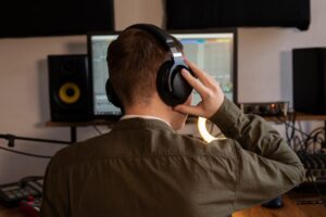 A person wearing headphones adjusts audio settings in a music production studio, with a computer and equipment in view.