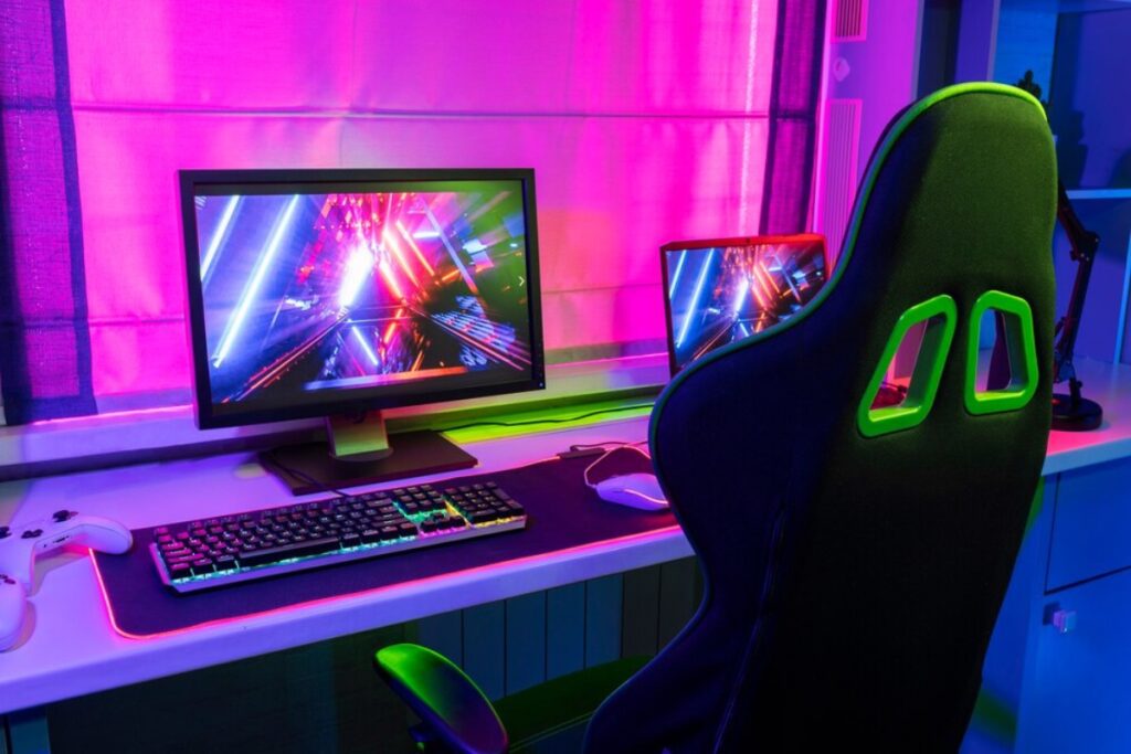A gaming setup featuring colorful monitors, a sleek gaming chair, and a backlit keyboard, all bathed in vibrant purple and green hues.