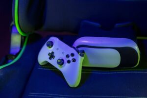 A white gaming controller rests on a blue gaming chair, with green and blue lighting enhancing the gaming atmosphere.