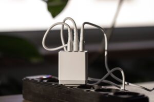 A compact white power adapter with multiple cables connected, plugged into a black power strip on a table.