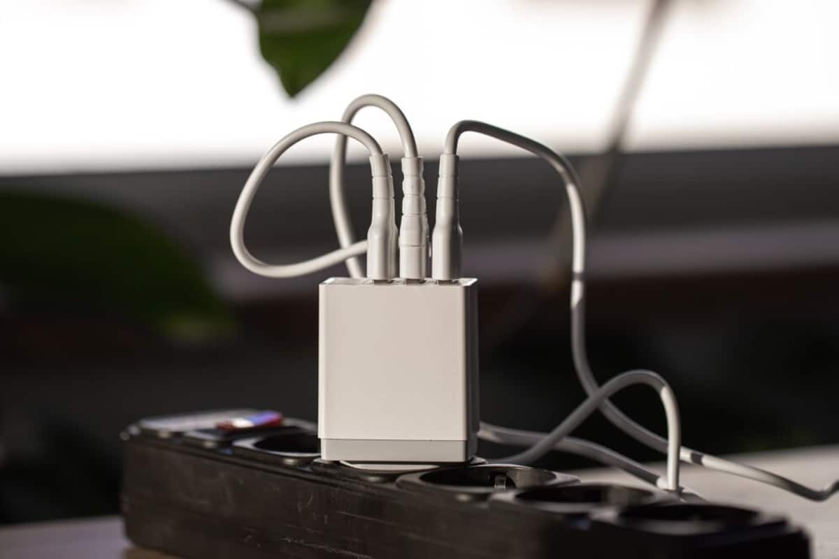 A compact white power adapter with multiple cables connected, plugged into a black power strip on a table.