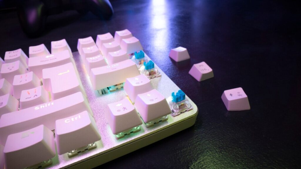 Close-up of a mechanical keyboard with white keycaps and blue switches, featuring some disassembled keys against a dark background.