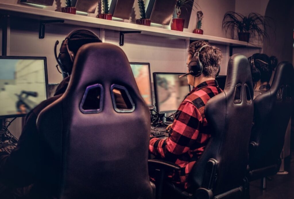 Three gamers wearing headphones are focused on their screens in a gaming room, with plants in the background adding a modern touch.