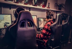 Three gamers wearing headphones are focused on their screens in a gaming room, with plants in the background adding a modern touch.