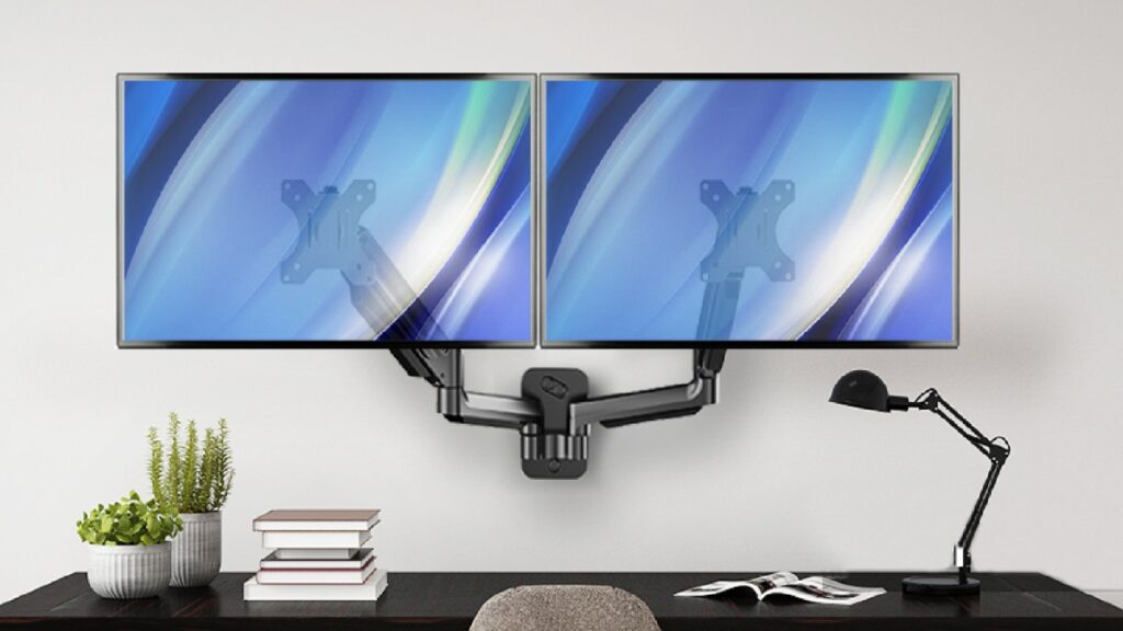 Dual monitors mounted on a sleek, adjustable arm above a dark desk with books, plants, and a desk lamp in a modern workspace.