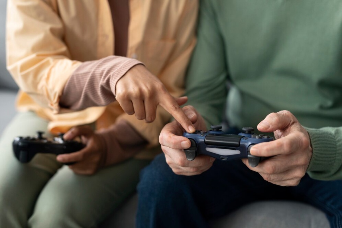 A close-up of two people playing video games together; one points at the controller while the other grips it attentively.