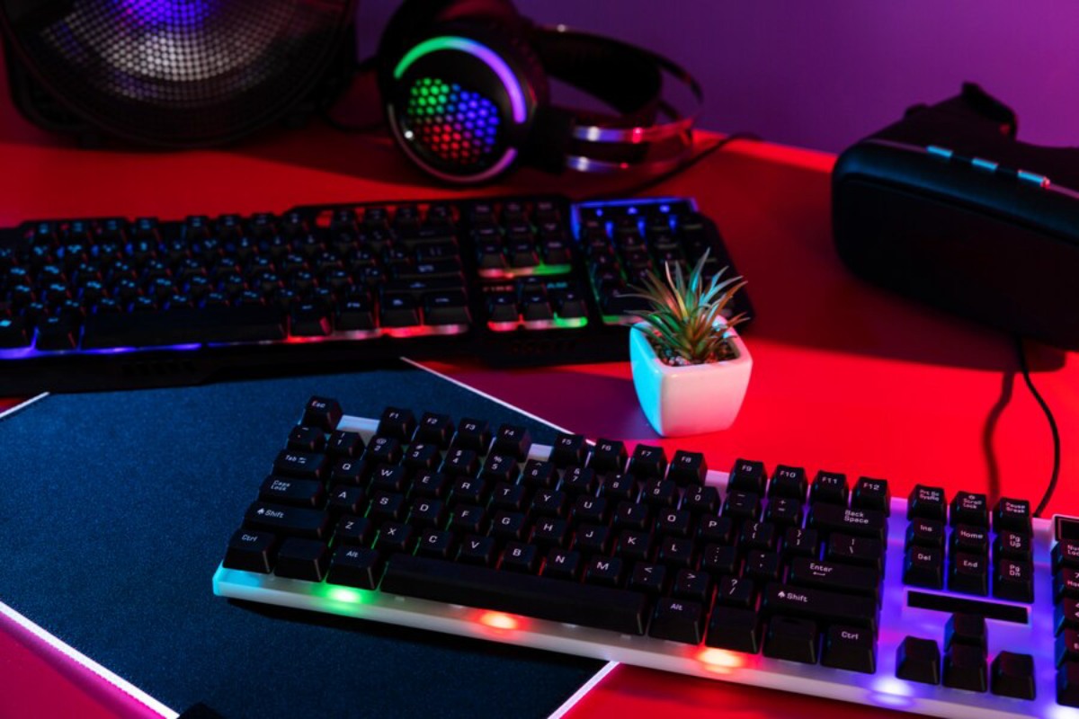 A colorful gaming setup featuring two illuminated keyboards, headphones, a small plant, and a VR headset on a vibrant red desk.