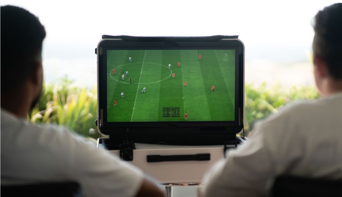 Two individuals sit side by side, focused on a video game screen displaying a soccer match in progress.