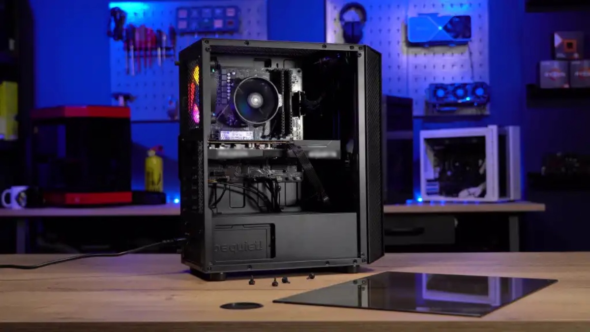 A sleek gaming PC case sits on a wooden desk, showcasing its internal components and colorful fans, with monitors and tools in the background.