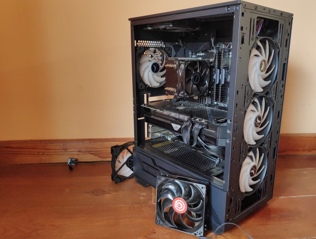 An open gaming PC case with several fans visible, showcasing components like a graphics card and cooling system, placed on a wooden floor.