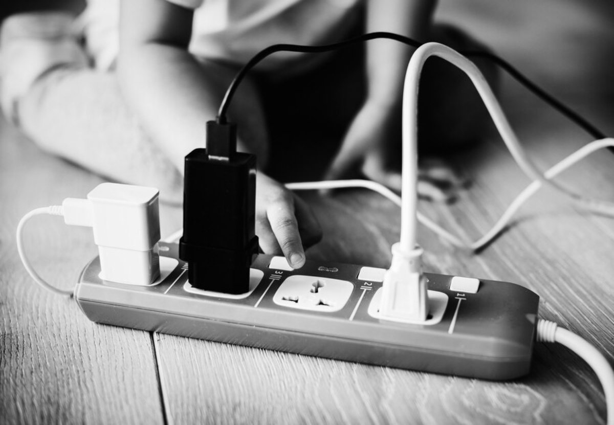 A child's hand reaches for a power strip with multiple plugged devices, highlighting safety concerns with electric outlets.