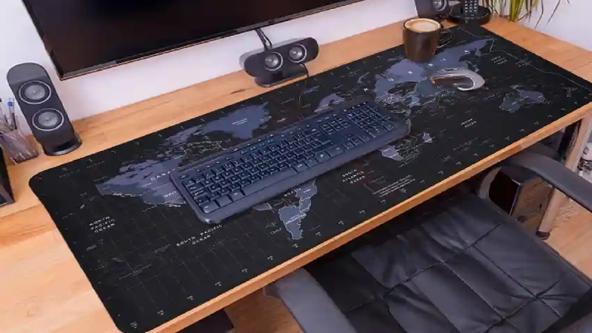 A desk with a black world map mouse pad, keyboard, speakers, and a coffee cup, creating a modern workspace aesthetic.
