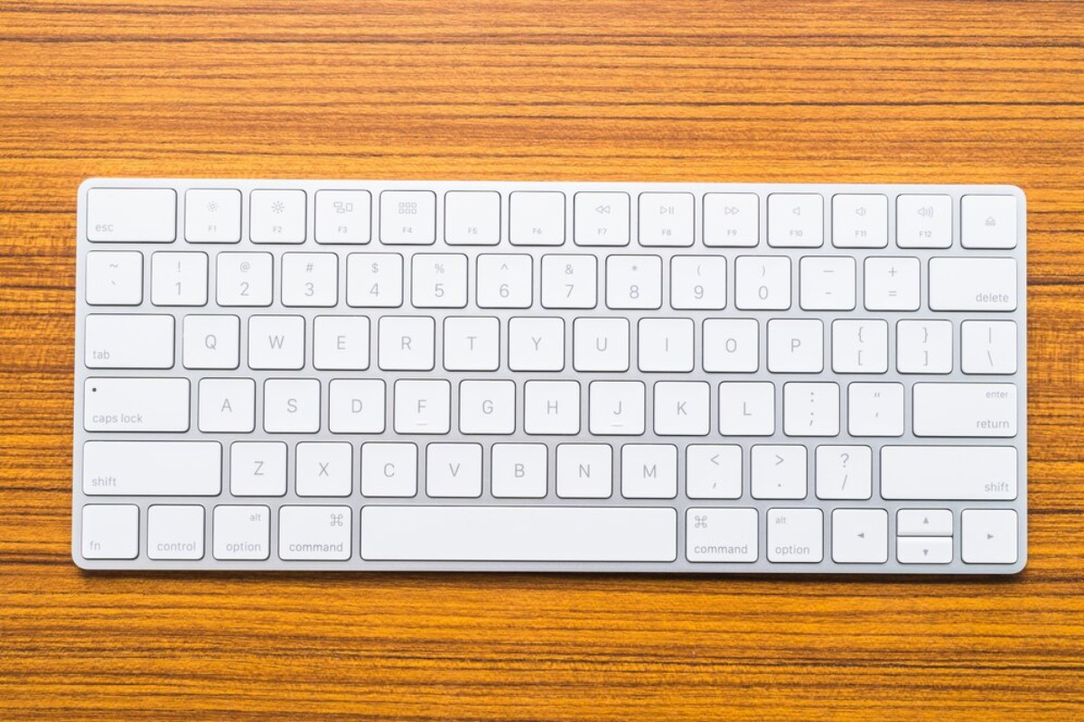 A white keyboard rests on a wooden table, featuring QWERTY layout and function keys, with a sleek and minimalist design.