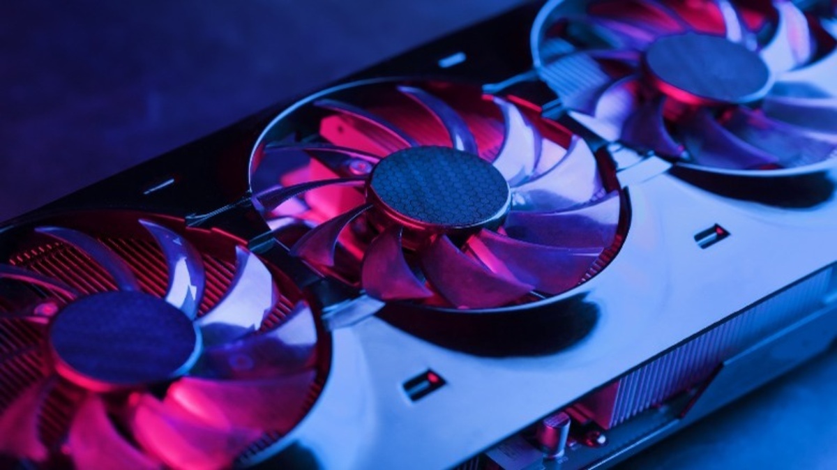Close-up of a computer graphics card with three illuminated cooling fans, showcasing a sleek metallic design and vibrant pink and blue lighting.