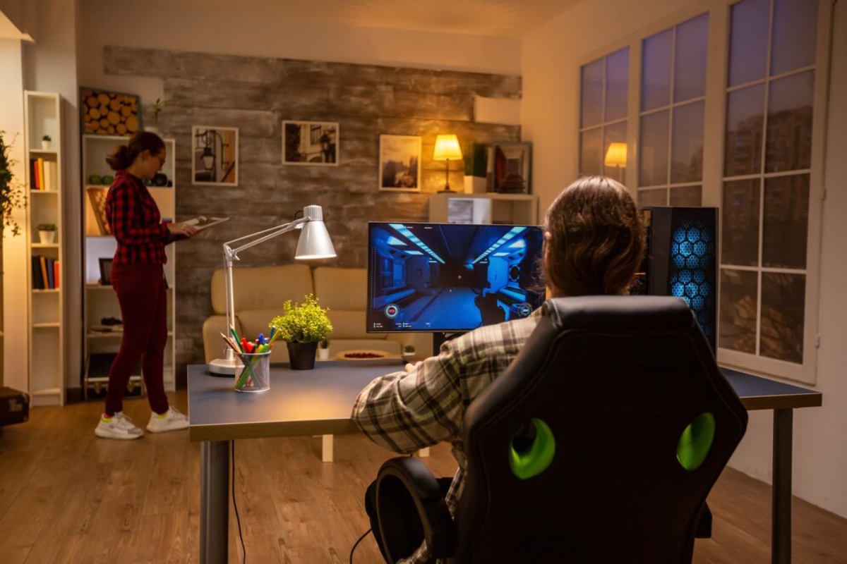 A gamer sits in a modern office, focused on a bright monitor displaying a video game scene, with decorative elements in the cozy room.