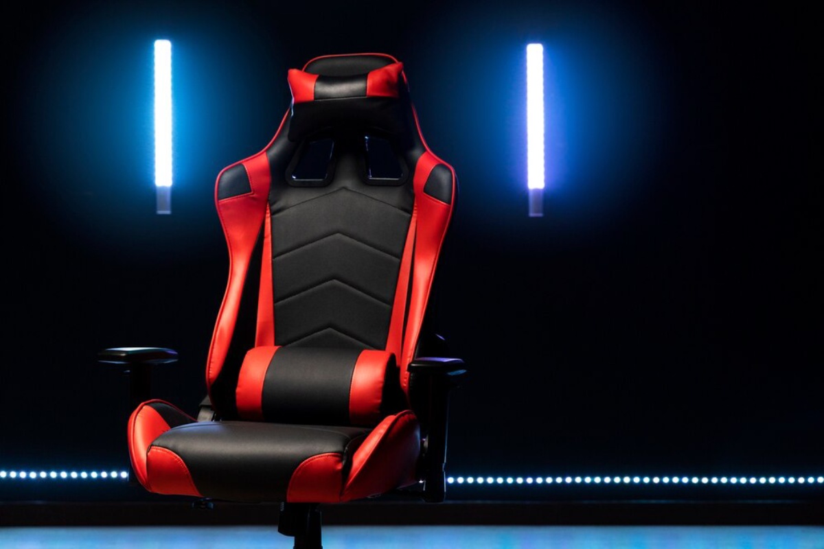 A sleek black and red gaming chair displayed against a dark background, illuminated by glowing blue lights.