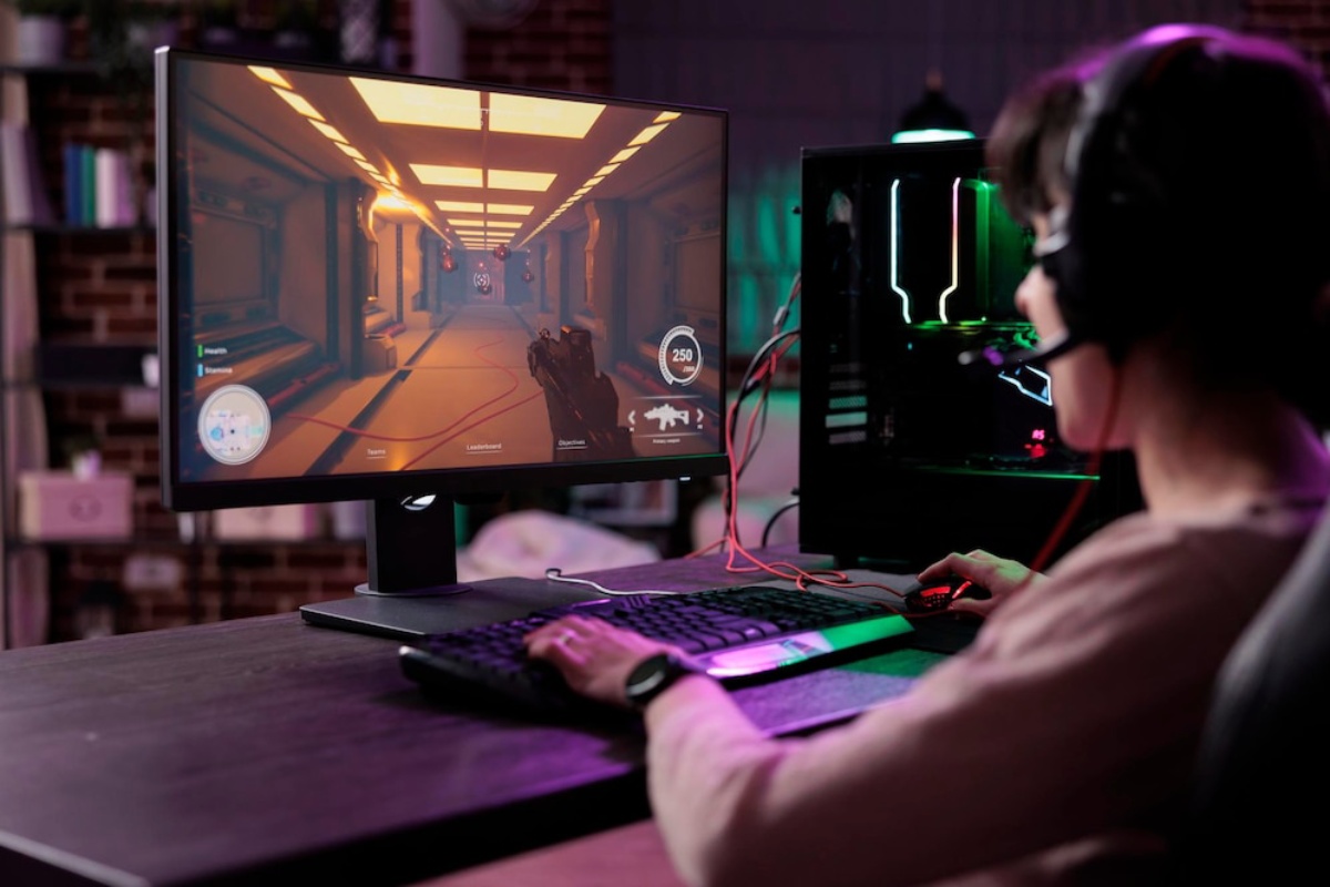 A gamer plays a first-person shooter on a computer monitor, wearing headphones and focused on the screen's colorful graphics.