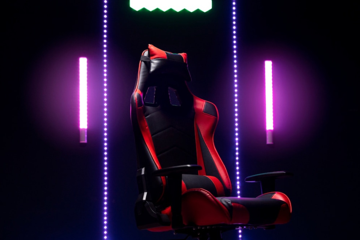 A sleek gaming chair with red and black upholstery, illuminated by colorful LED lights in a dark setting.