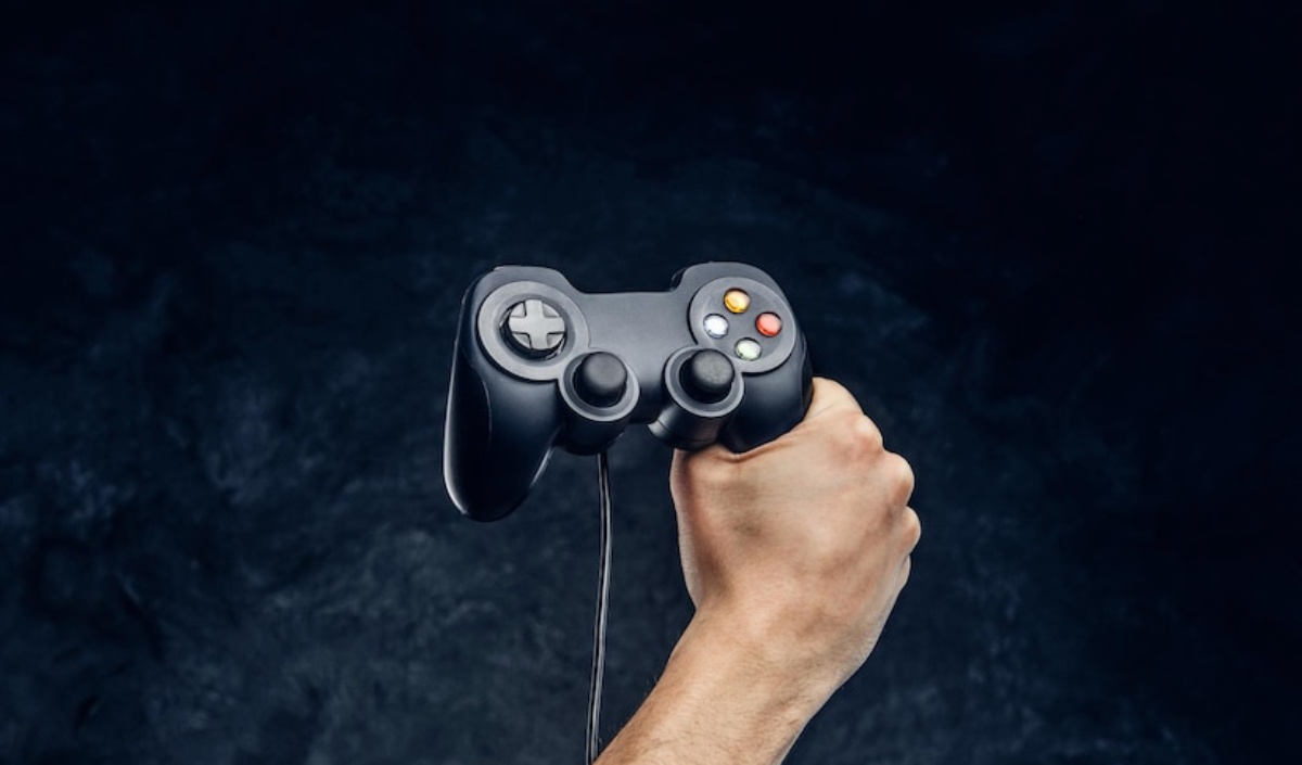 A person holds a black video game controller with buttons and joysticks, set against a dark background.