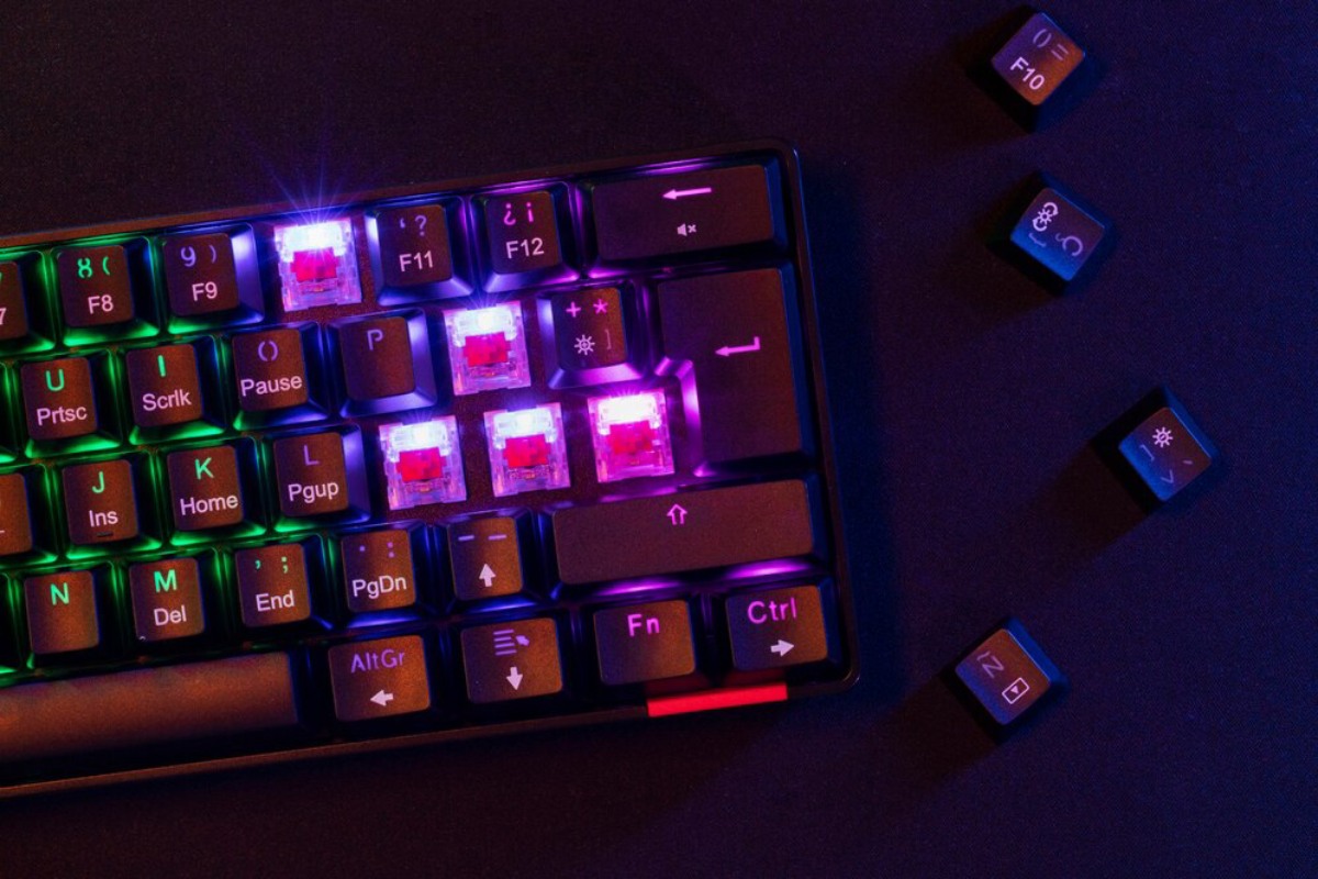 A close-up of a backlit mechanical keyboard with colorful keys, featuring some removed keycaps resting beside it.