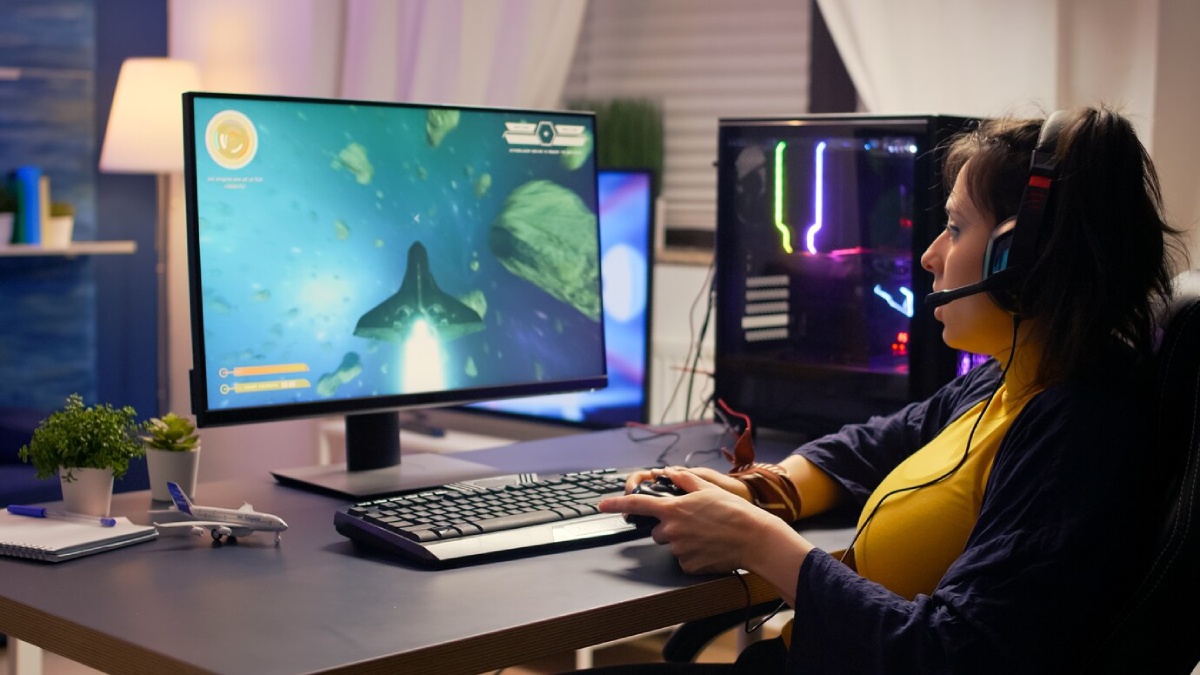 A person sits at a desk gaming on a computer with a vibrant space-themed display and a gaming setup featuring colorful lights.