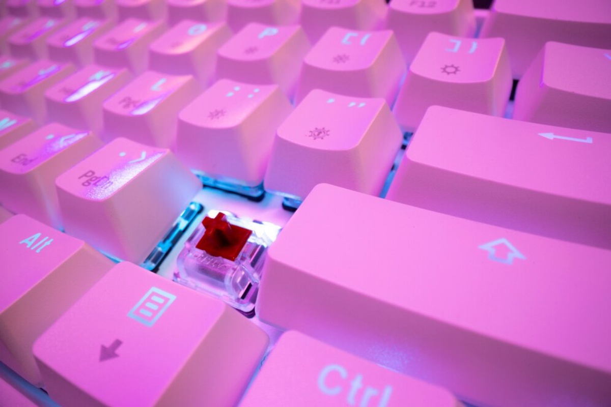 Close-up of a pink backlit keyboard, featuring a red mechanical key switch, with glowing keys and a vibrant aesthetic.
