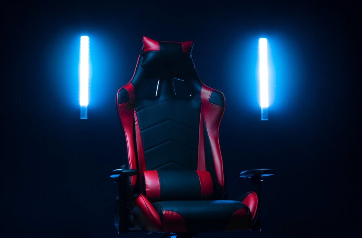 A sleek gaming chair with red and black upholstery, illuminated by colorful LED lights in a dark setting.