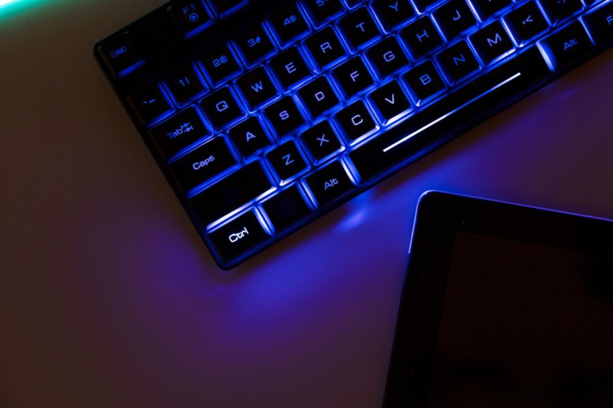 Close-up of a glowing blue keyboard with a sleek design, next to a dark tablet on a minimalistic surface.