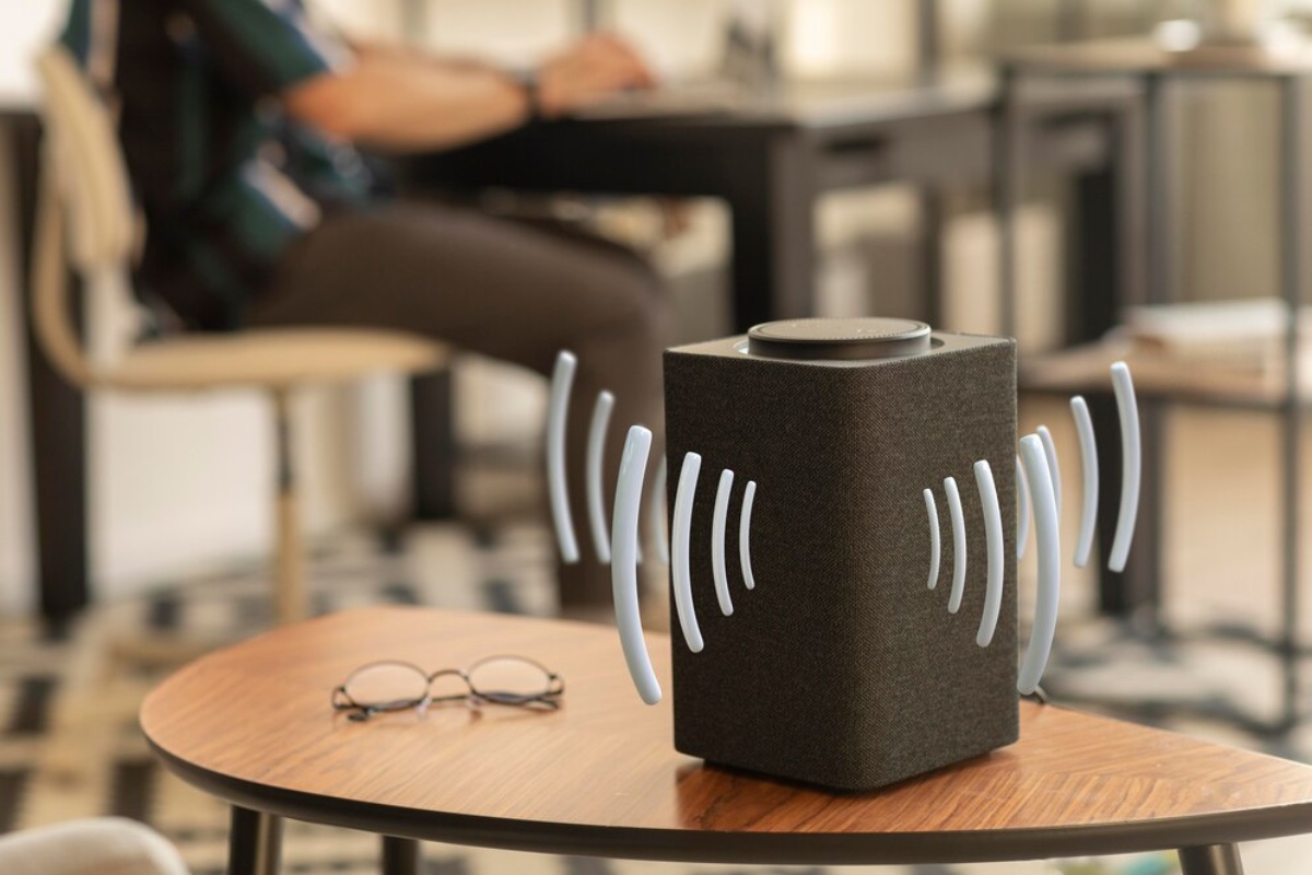 A stylish speaker on a table emits sound waves, while a person works in the background, creating a cozy atmosphere.