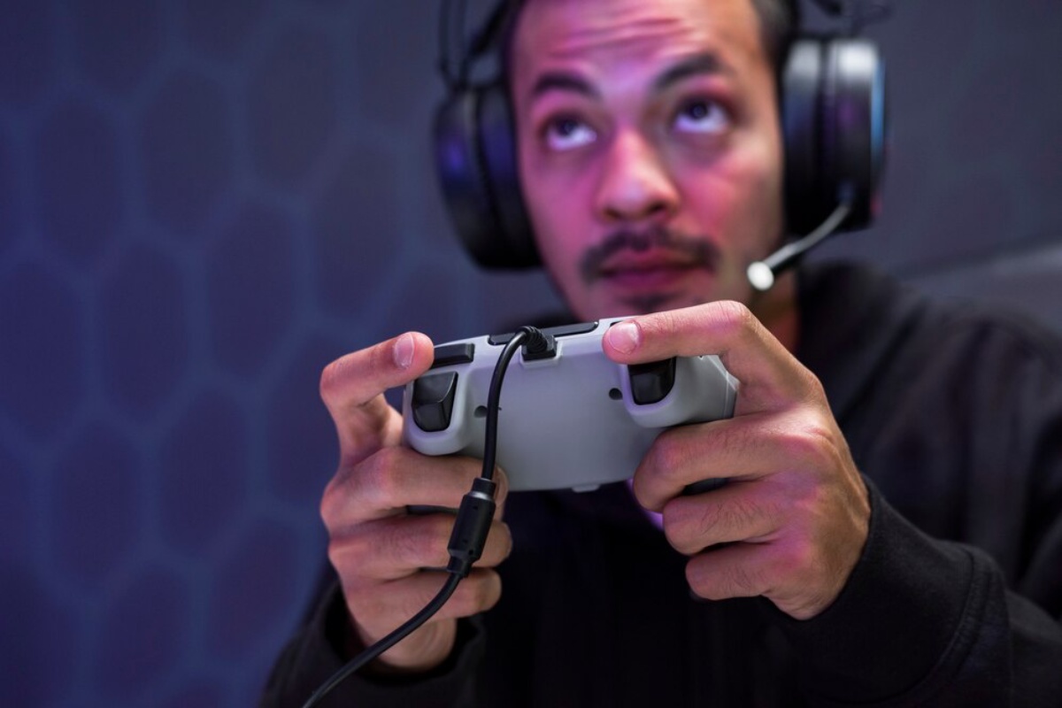 A person wearing headphones grips a game controller, focused on gameplay against a stylish, modern background.
