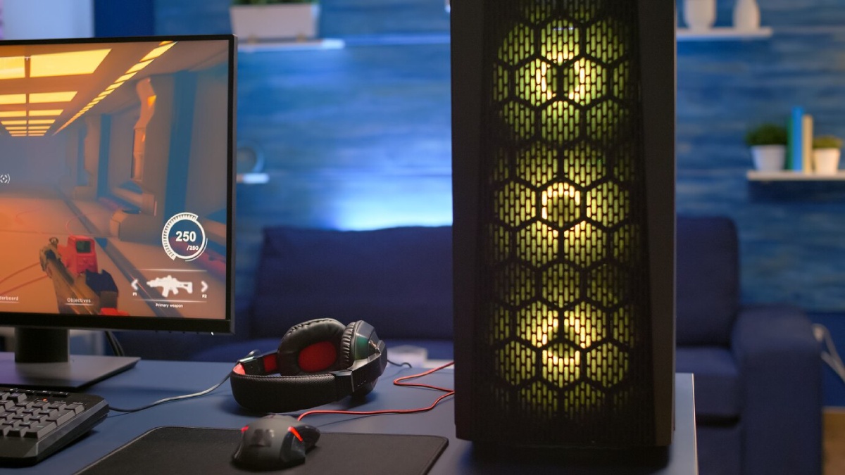 A gaming setup featuring a monitor displaying a first-person shooter, with a stylish PC tower, headset, and mouse on a desk.