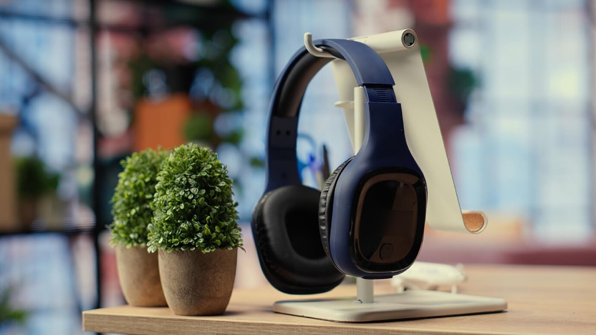 A pair of navy headphones rests on a sleek stand beside two small potted plants, against a bright, blurred indoor background.