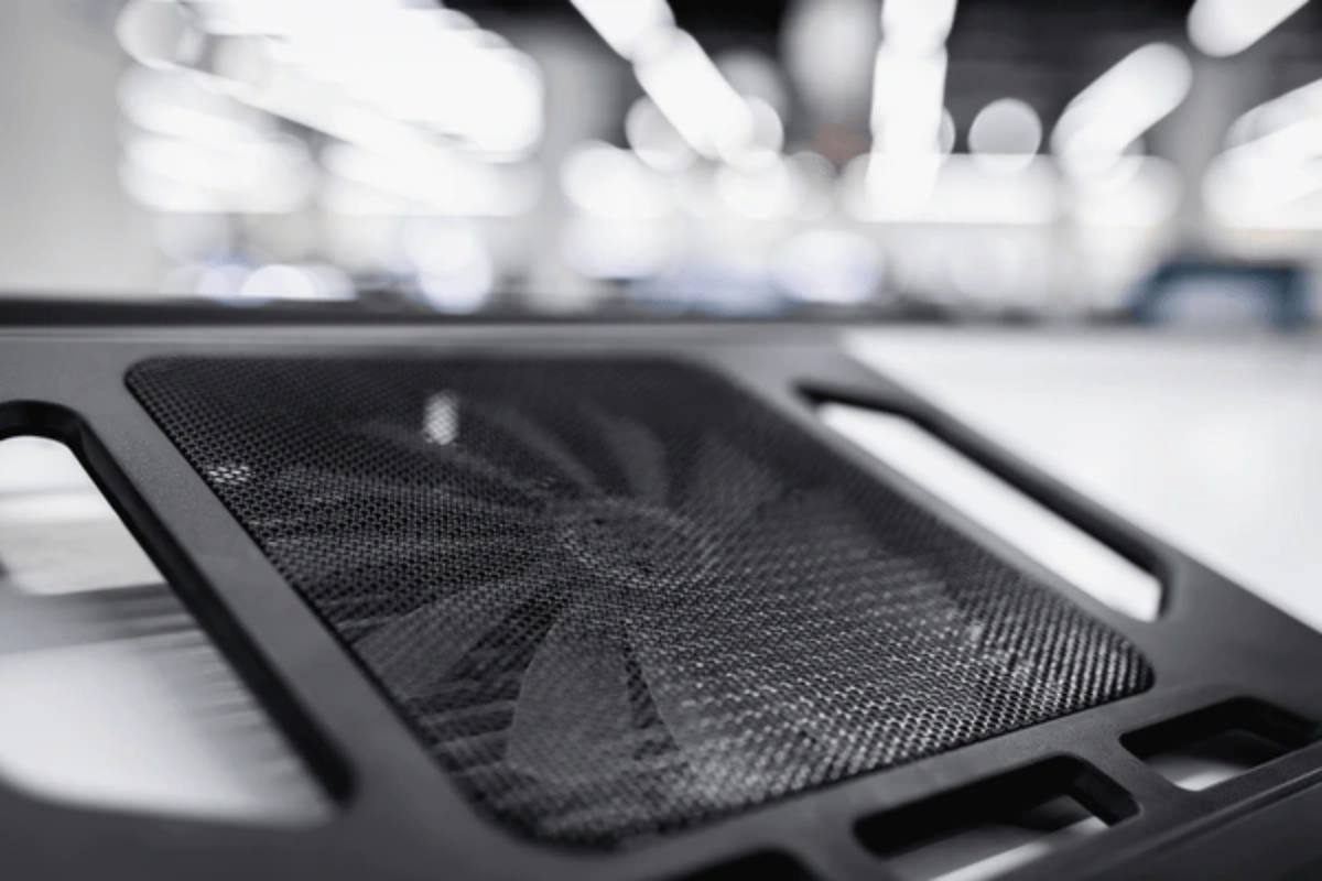 Close-up of a black mesh laptop cooling pad with a visible fan, set against a blurred bright background.